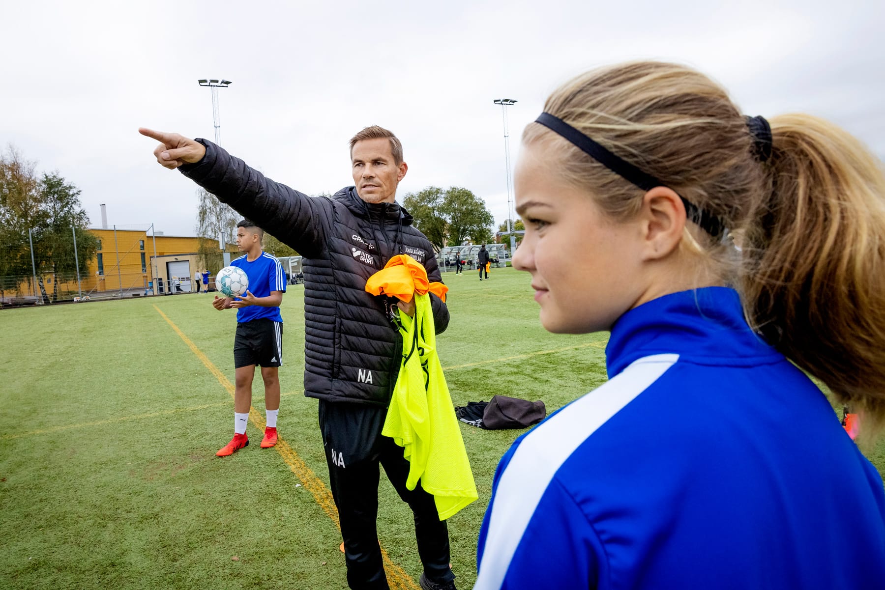 Niclas Alexandersson instruerar en grupp ungdomar på fotbollsplanen vid Änglagårdsskolan. Foto: Emelie Asplund